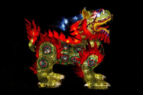 A brightly lit, colorful dragon sculpture with intricate patterns, set against a dark background.