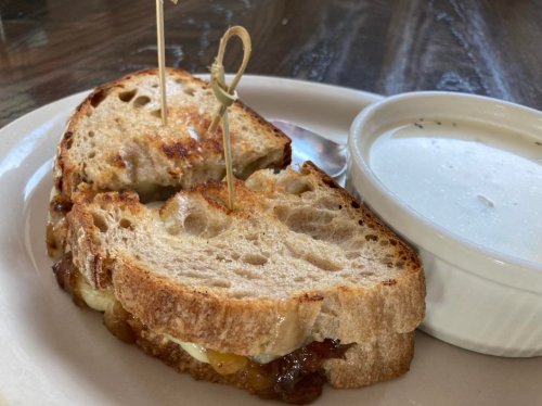 A toasted sandwich with melted cheese and caramelized onions, served with a small bowl of creamy soup.