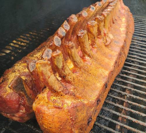 A large, seasoned rack of ribs cooking on a grill, showcasing a golden-brown crust and visible bone structure.