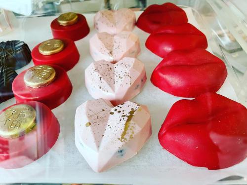 A display of heart-shaped and lip-shaped chocolates in pink and red, some with gold accents, arranged neatly.