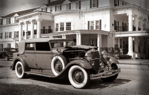 A vintage car parked in front of a grand, historic building with white columns and a classic architectural style.