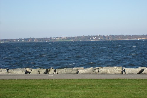 A view of a choppy sea with a rocky shoreline and distant land under a clear blue sky.