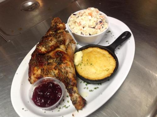 A plate featuring roasted chicken, coleslaw, cornbread, and a side of cranberry sauce.
