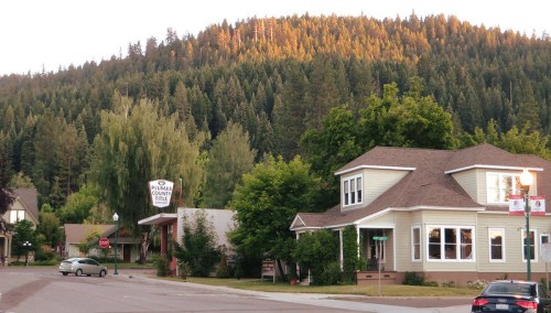 A quaint town scene with a two-story house, trees, and a mountain backdrop illuminated by the setting sun.