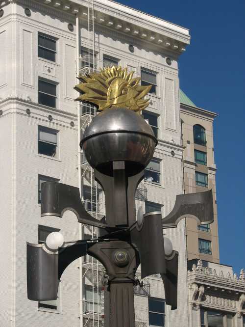 A decorative street lamp with a sun motif atop, set against a backdrop of buildings and a clear blue sky.