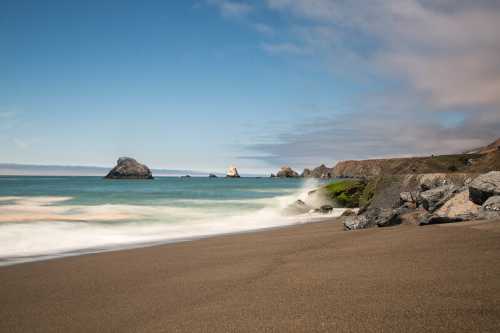 A serene beach scene with gentle waves, rocky formations, and a clear blue sky.