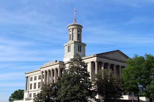 Historic building with a tall tower, surrounded by trees and a clear blue sky.