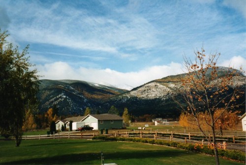 A scenic view of mountains with snow-capped peaks, surrounded by autumn trees and a rural landscape.