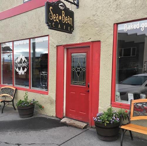Exterior of Sea Bean Café featuring a red door, flower pots, and large windows with a cozy, inviting atmosphere.