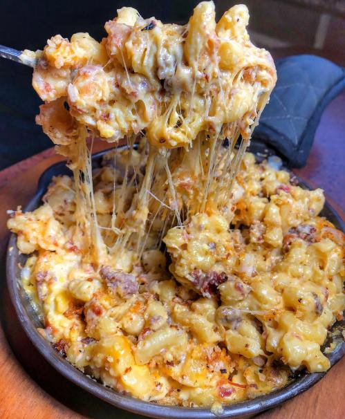 A cheesy, baked macaroni dish with gooey melted cheese and crispy topping, served in a small cast-iron skillet.