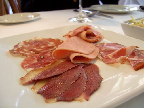 A plate of assorted cured meats, including salami, ham, and prosciutto, arranged neatly on a white dish.