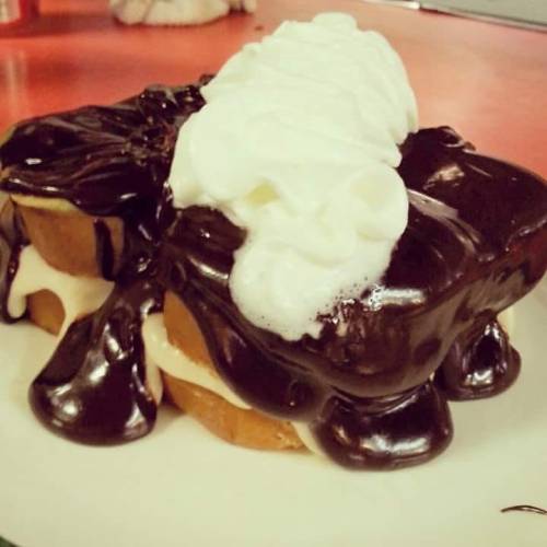 A dessert featuring two layers of cake filled with cream, topped with chocolate sauce and whipped cream.
