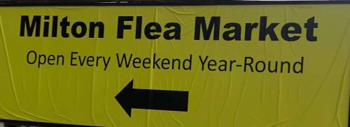Sign for Milton Flea Market, open every weekend year-round, with an arrow pointing left.