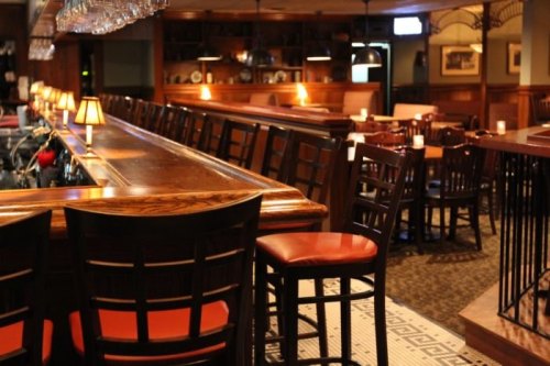 A cozy bar interior with wooden furniture, dim lighting, and empty tables, creating a warm, inviting atmosphere.