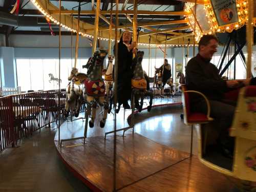 A vintage carousel with riders on horses, featuring bright lights and a cheerful atmosphere.