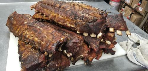 A stack of smoked, charred ribs on a cutting board, showcasing a rich, dark crust and visible bones.