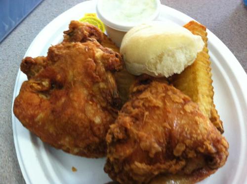 A plate of fried chicken, a roll, and a side of green sauce, served on a white disposable plate.