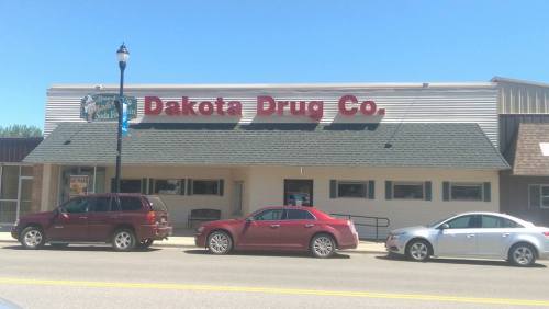 Exterior of Dakota Drug Co. building with a clear blue sky and parked cars in front.