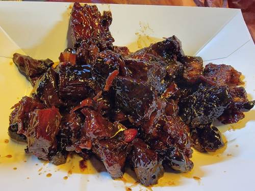 A pile of dark, glossy, caramelized meat pieces on a white tray, glistening with sauce.