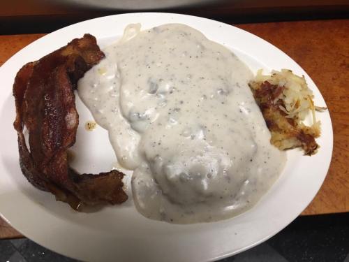 A plate of biscuits and gravy, crispy bacon, and hash browns.