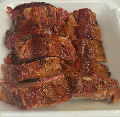 Sliced, smoked meat arranged in a white takeout container, showcasing a caramelized, crispy exterior.