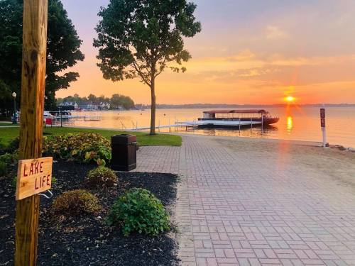 A serene lakeside view at sunset, featuring a sign that reads "Lake Life," with boats and trees in the background.