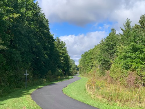 A winding path through lush green trees under a partly cloudy sky.