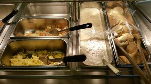 A buffet serving station with trays of scrambled eggs, gravy, and biscuits, with serving utensils visible.