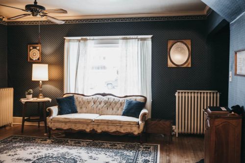 Cozy living room with a vintage sofa, lamp, and patterned wallpaper, featuring a large window and decorative radiator.