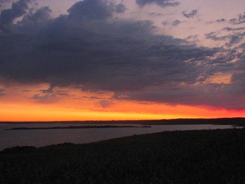 A vibrant sunset over a calm lake, with dramatic clouds and a colorful sky reflecting warm hues.