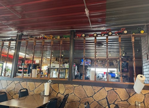 Interior of a rustic restaurant featuring wooden decor, a stone wall, and toy tractors displayed on a shelf above.