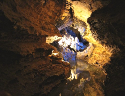A dimly lit cave with rocky walls and a calm water surface reflecting light.