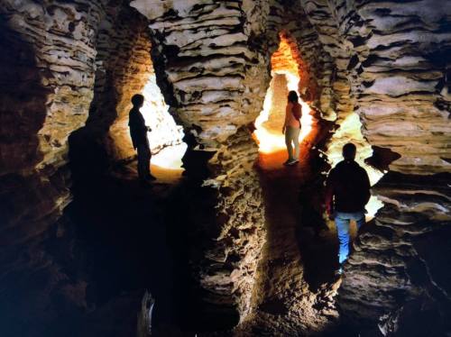 Three people explore a rocky cave, illuminated by warm light, highlighting the textured stone formations.