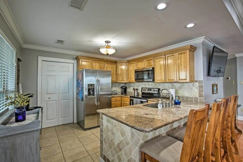 Modern kitchen with wooden cabinets, stainless steel appliances, and a granite island with bar stools. Bright and spacious.