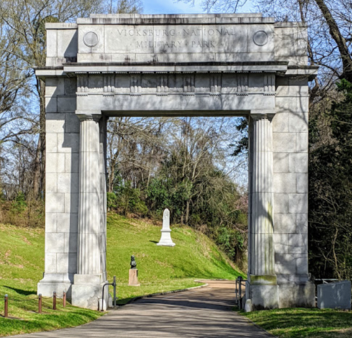 Stone archway at Vicksburg National Military Park, leading to a statue in a green, tree-lined area.