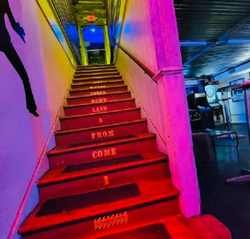 Colorful staircase with artistic lighting, featuring text on the steps: "FROM A JUMBO LAND COME I."
