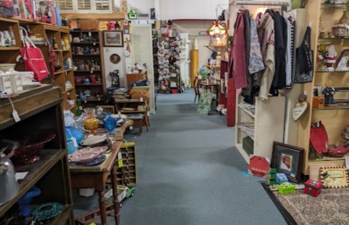 A cozy antique shop aisle lined with various vintage items, furniture, and clothing on display.