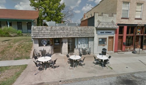 A small building with a shingled roof, featuring outdoor tables and a sign for a bail bonds service.