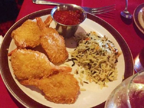 A plate with four golden fried shrimp, a small cup of marinara sauce, and a serving of seasoned rice.