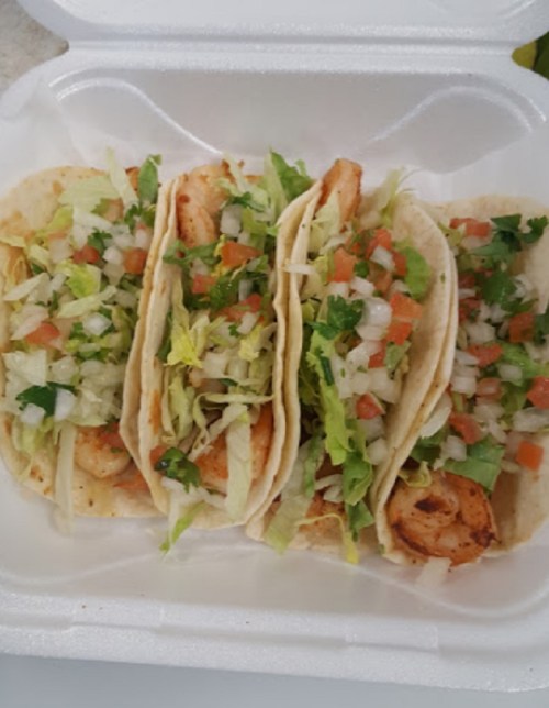Three tacos filled with grilled chicken, lettuce, tomatoes, and onions in a takeout container.