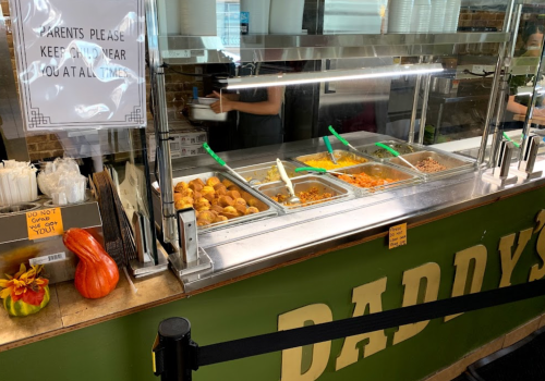 A food counter with various dishes, a sign for parents, and a decorative pumpkin on the side.