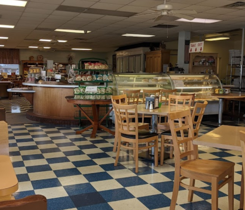 A cozy café interior with wooden tables, chairs, and a display case filled with food, featuring a checkered floor.
