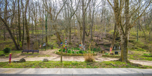A serene wooded area with benches, colorful sculptures, and a path winding through trees in early spring.