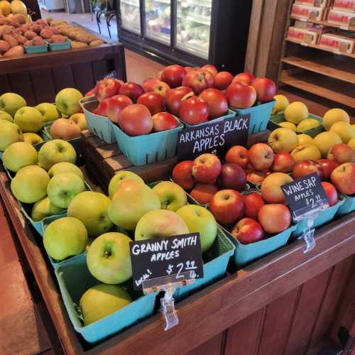 A display of various apples, including Granny Smith and Arkansas Black, in baskets at a market. Price tags visible.