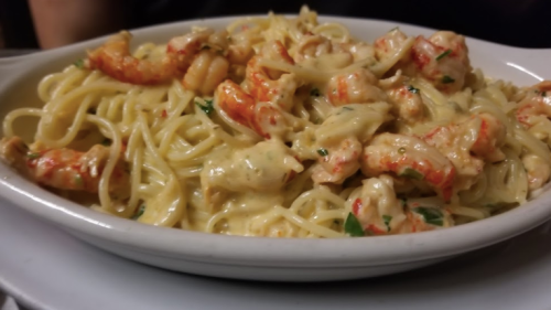 A plate of creamy pasta with shrimp and herbs, garnished and served in a white dish.