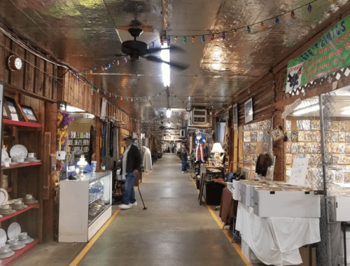 A long, narrow aisle in a vintage shop, lined with displays, colorful lights, and a person browsing.