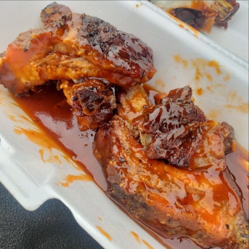 Close-up of tender, glazed barbecue ribs in a takeout container, coated in a rich, sticky sauce.