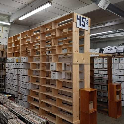 A wooden shelving unit filled with boxes labeled "45s" in a record store, with vinyl records visible in the foreground.