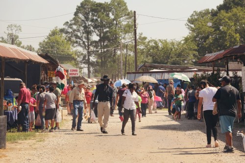 A bustling outdoor market scene with people walking, vendors, and colorful umbrellas on a sunny day.