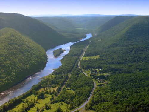 Aerial view of a winding river surrounded by lush green hills and valleys under a clear blue sky.